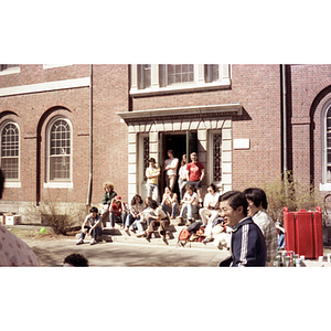 Young adults gather on the steps of a building to watch a mime perform