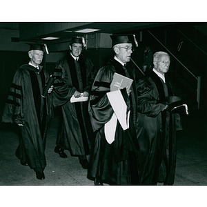 Honorary degree recipients and their escorts in caps and gowns walking towards the commencement ceremony