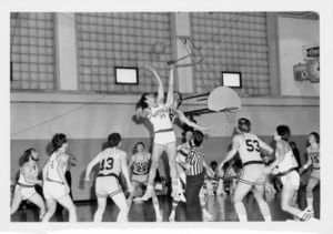 Suffolk University men's basketball player Chris Tsiotos (#33) goes up for a jump ball, as other players look on, during a Suffolk versus Lowell State game, 1975
