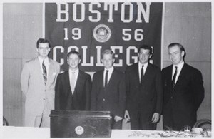Five members of the Boston College Class of 1956 standing in front of college banner