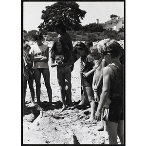 A woman and a group of girls look at a sand castle on a beach