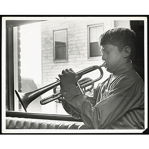 A boy plays a trumpet next to a window