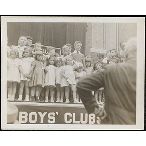 Participants standing on the outdoor stage with their brothers during a Boys' Club Little Sister Contest