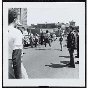 Race officials and spectators watch two teenage boys complete the Roxbury Road Race