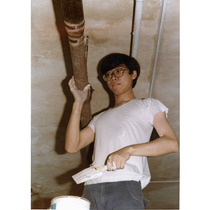 Chinese Progressive Association member paints a ceiling pipe as part of a building renovation project