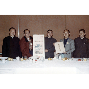 Henry Wong stands with four other men behind a banquet table to hold up artwork