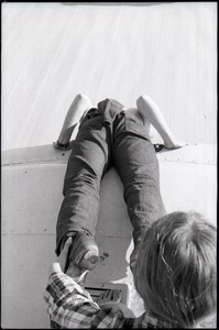 Woman holding the ankles of a person lying on top of the Free Spirit Press bus and leaning over the edge