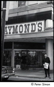 Bill Baird, contraception rights advocate, standing outside Raymond's Restaurant, holding a copy of the day's newspaper