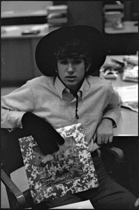 At the Boston University News Office: Peter Simon wearing hat and glove and holding copy of Rolling Stones', 'Their Satanic Majesties Request'