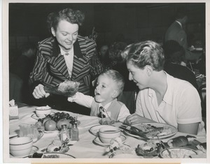 Two women helping young client eating turkey at Thanksgiving dinner