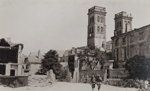 Soldiers walking along a street past damaged buildings