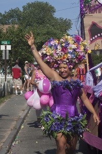 Marcher with large floral headress along side the parade float for Priscilla, Queen of the Cape : Provincetown Carnival parade