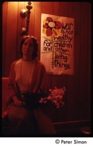 Woman with flowers seated in front of antiwar poster (War is not healthy for children and other living things), Tree Frog Farm commune
