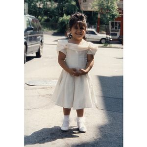 A little girl wears a dress and stands in the street