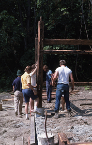 Jim Skinner (yellow shirt on left) and Peter Jensen (white shirt, back to camera on right) righting southeast corner post at at Moon Barn Raising at entrance to Hopkins Forest on 2 August 1975.