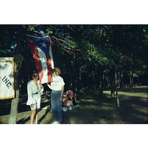 Two women stand in front of a Puerto Rican flag at a Festival Puertorriqueño picnic event