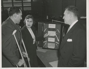 A woman speaks with a man on crutches about vocational opportunities while another man looks on