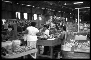 Shopper examining produce, vendors, in the old marketplace, Belize City