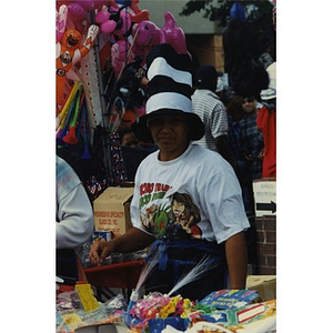 Woman in a tall black and white striped cloth hat staffs a display of merchandise at Festival Betances.