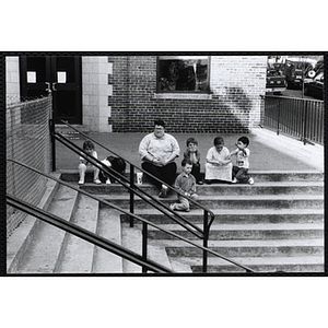 A woman sitting on the stairs with six boys and girls outside the Charlestown Boys & Girls Club building