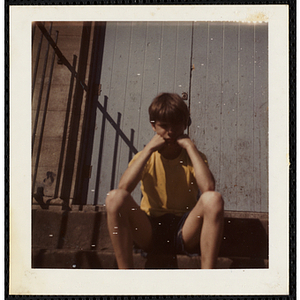 A boy sitting on the front steps at the South Boston Boys' Club, resting his head on his hands