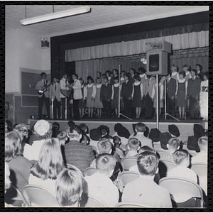 Boys' Clubs of Boston choral group performs on the stage in the South Boston Clubhouse. A caption on the back of the photograph states "Sing-out"