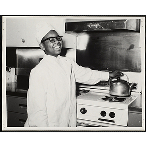 A member of the Tom Pappas Chefs' Club poses next to a stove and kettle in a kitchen