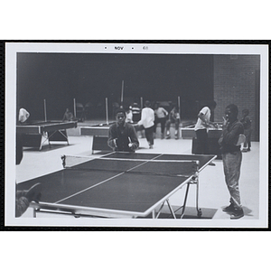 Two boys play table tennis in a hall as another boy looks on