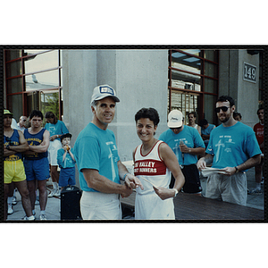 A woman receives a certificate from a man as she shakes his hand during the Battle of Bunker Hill Road Race