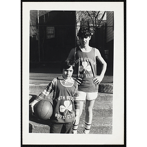 Two boys wearing South Boston Boys' Club jerseys pose for a shot on a playground's basketball court
