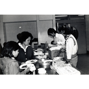 Chinese Americans standing around a table, getting food at a potluck buffet at the 29th anniversary celebration of the People's Republic of China, held at the Josiah Quincy School