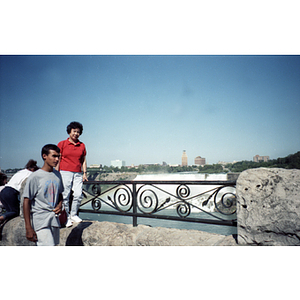 Woman stands on a stone wall near Niagara Falls, while a young man passes by