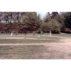 Girl crouches to catch a ball during a kickball game in a grassy park