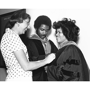 A woman and a man help a Law School graduate with her outfit at commencement