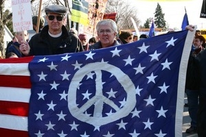 Marchers holding an American flag with a peace symbol overlaying the field of stars: rally and march against the Iraq War