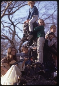 Judy Collins seated at the base of a statue, playing guitar for children