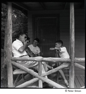 Camp Arcadia: camper talking with adults, seated on a cabin porch