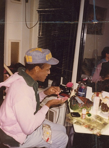 A Photograph of Marsha P. Johnson Sitting at a Side Table Applying her Makeup
