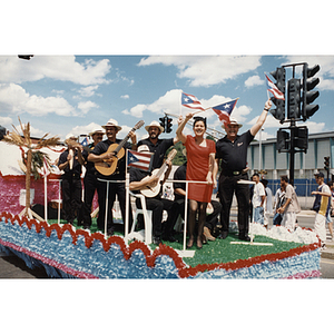 Several people stand on a float, waving Puerto Rican flags and playing instruments, at the Festival Puertorriqueño