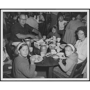 Family seated around table eating at unidentified camp
