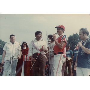 A man speaks into a microphone and holds a large trophy at the Festival Puertorriqueño