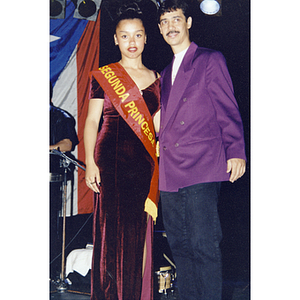 Damaris Padilla is wearing a sash and standing next to Eddie Santiago on stage at the Festival Puertorriqueño