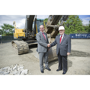 President Joseph E. Aoun and Dr. George J. Kostas shake hands in front of an excavator at the groundbreaking site for the George J. Kostas Research Institute for Homeland Security