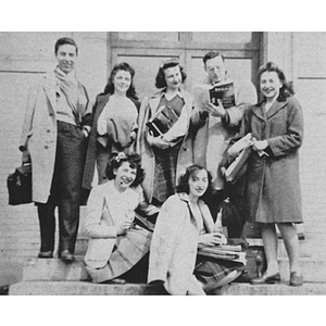 Seven students pose on steps holding books