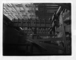 View of construction under a building, looking out at beams and a wood fence