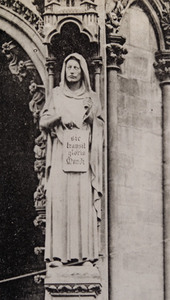 Close-up view of a church exterior, showing a stone statue of a robed figure holding a tablet reading "sic transit gloria mundi", Metz
