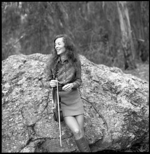 Woman with a fiddle, posed on a granite boulder in a eucalyptus grove