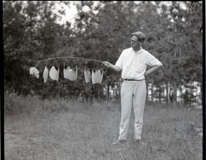 George Allan England holding a stick suspending a series of oversized visors