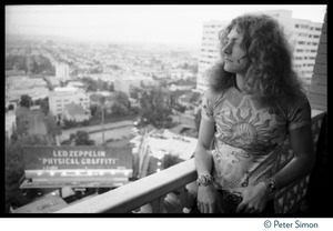 Robert Plant looking out from the balcony of his room at the Riot House, a billboard advertising Led Zeppelin's new album Physical Graffiti in the background