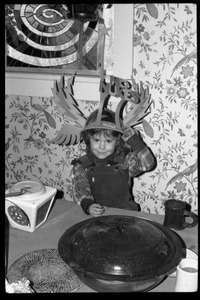 Child seated at a table, wearing a winged No Nukes headdress, Montague Farm commune